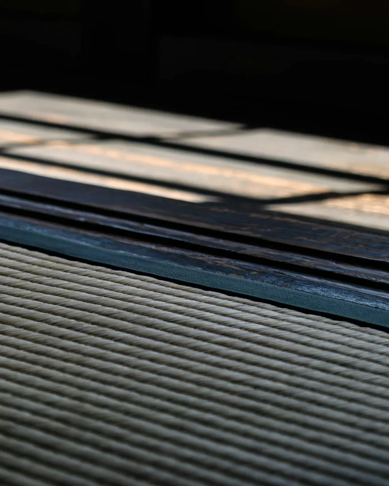Low light across a tatami floor, where the woven rush meets its cloth edging